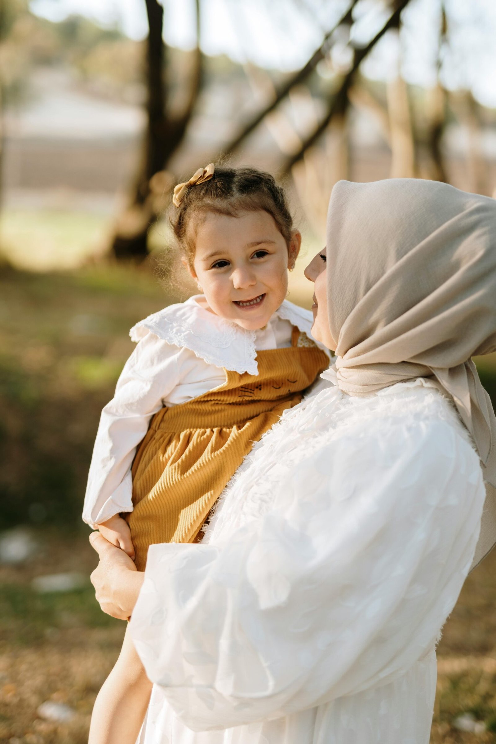 A loving mother holding her smiling daughter in a vibrant outdoor setting.